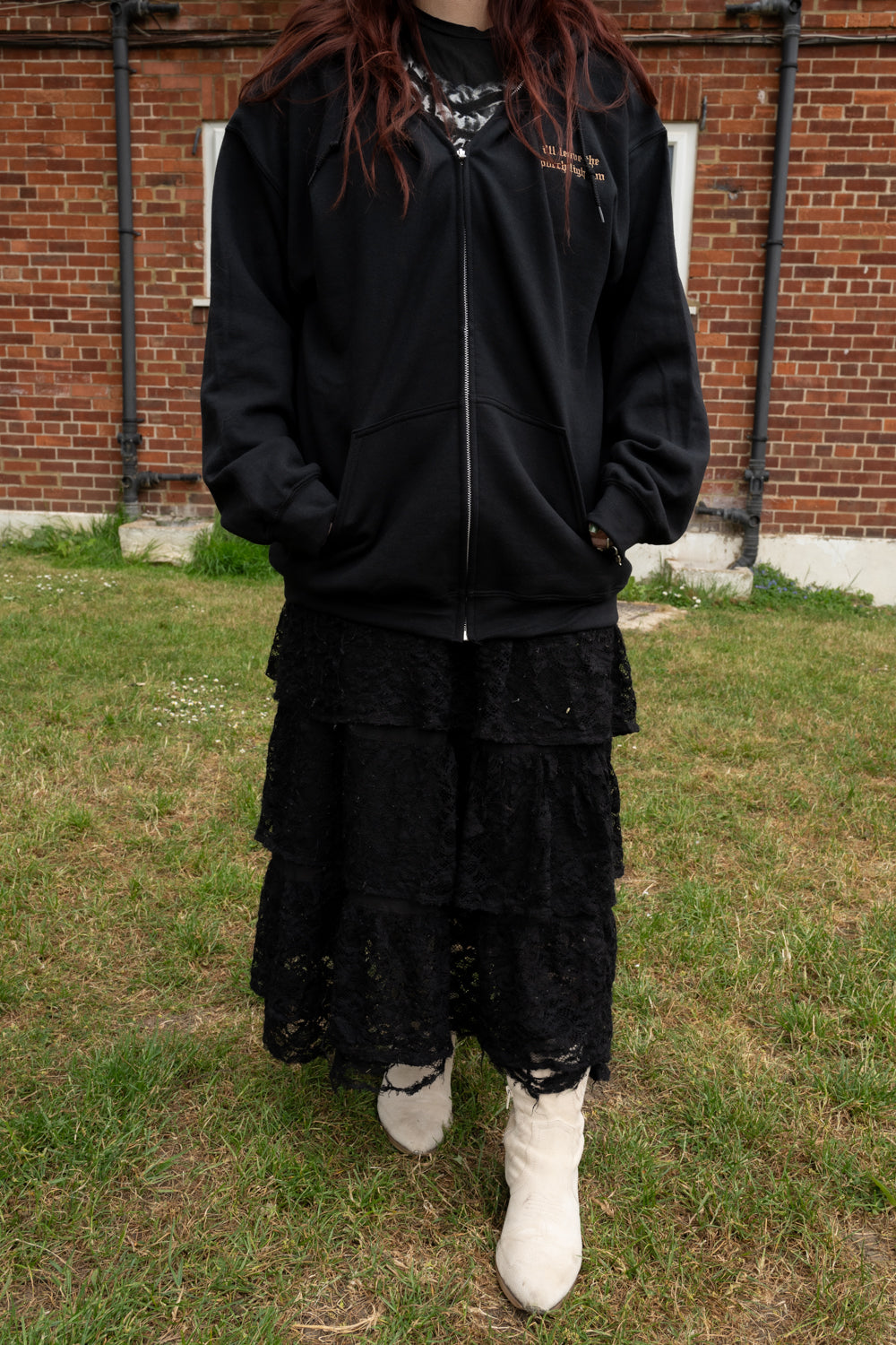 Black fleece lined zip-up hoodie styled for a Noah Kahan concert with a tiered black skirt and white cowboy boots, worn as a warm layer for an outdoor show.