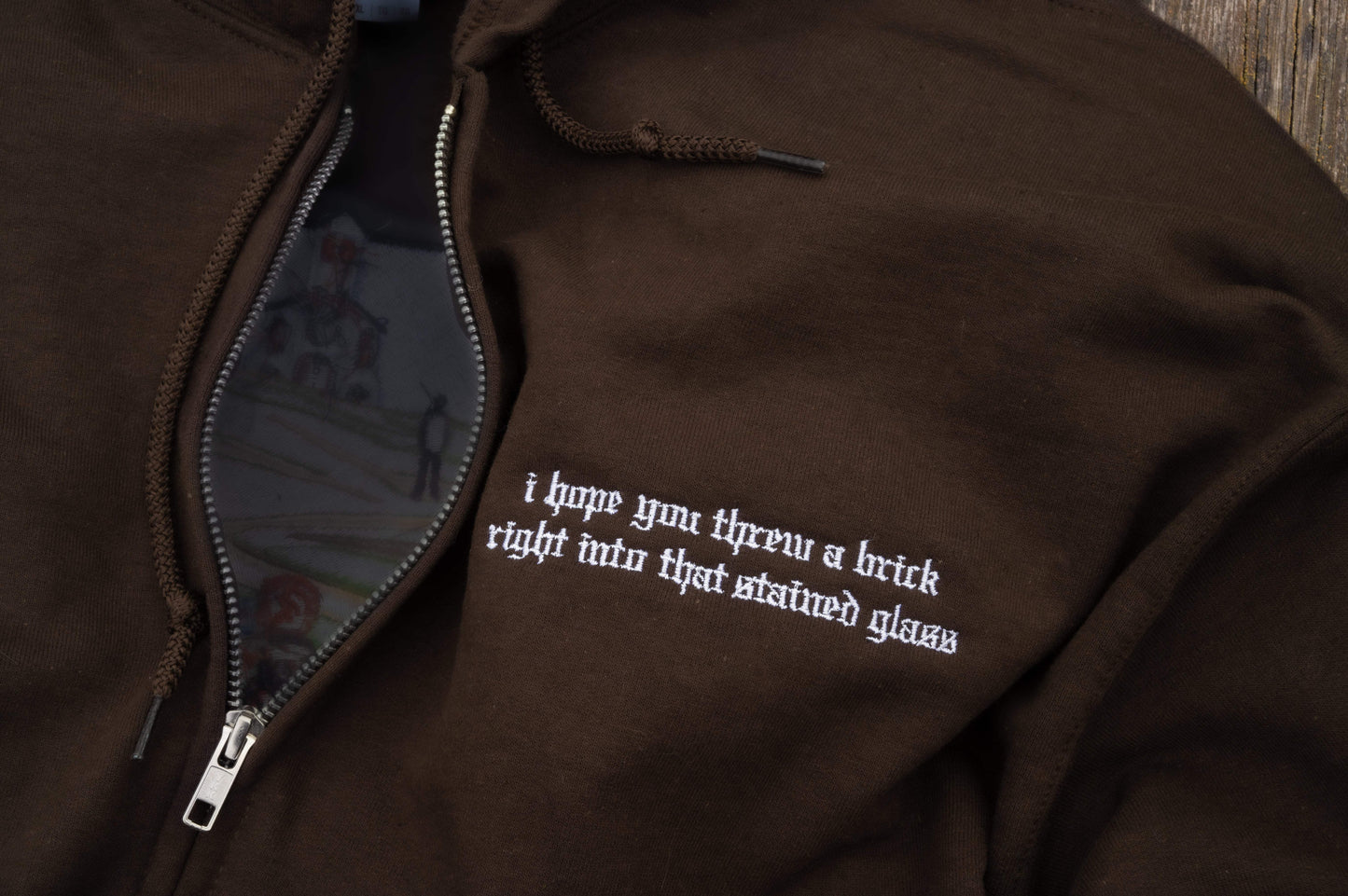 Flat lay of brown zip-up hoodie, silver full-zip hardware, drawstring hood, ribbed cuffs and hem, kangaroo pouch pockets, left-chest lyric embroidery -Noah Kahan The Great Divide inspired embroidered hoodie